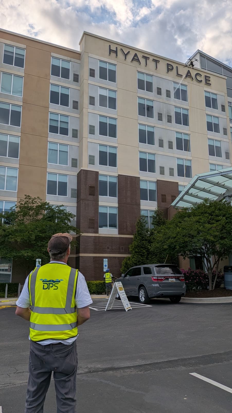 A Drone Precision Solutions pilot flying a cleaning drone up the facade of a multi-story Hyatt Place hotel.
