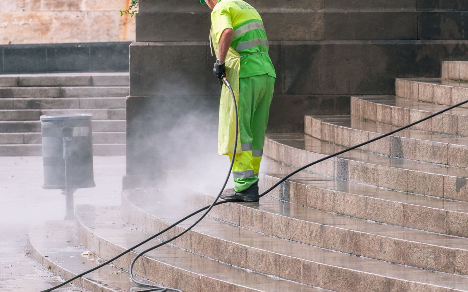 Pressure washing a set of concrete steps, cleaned stone showing against the dirty surface