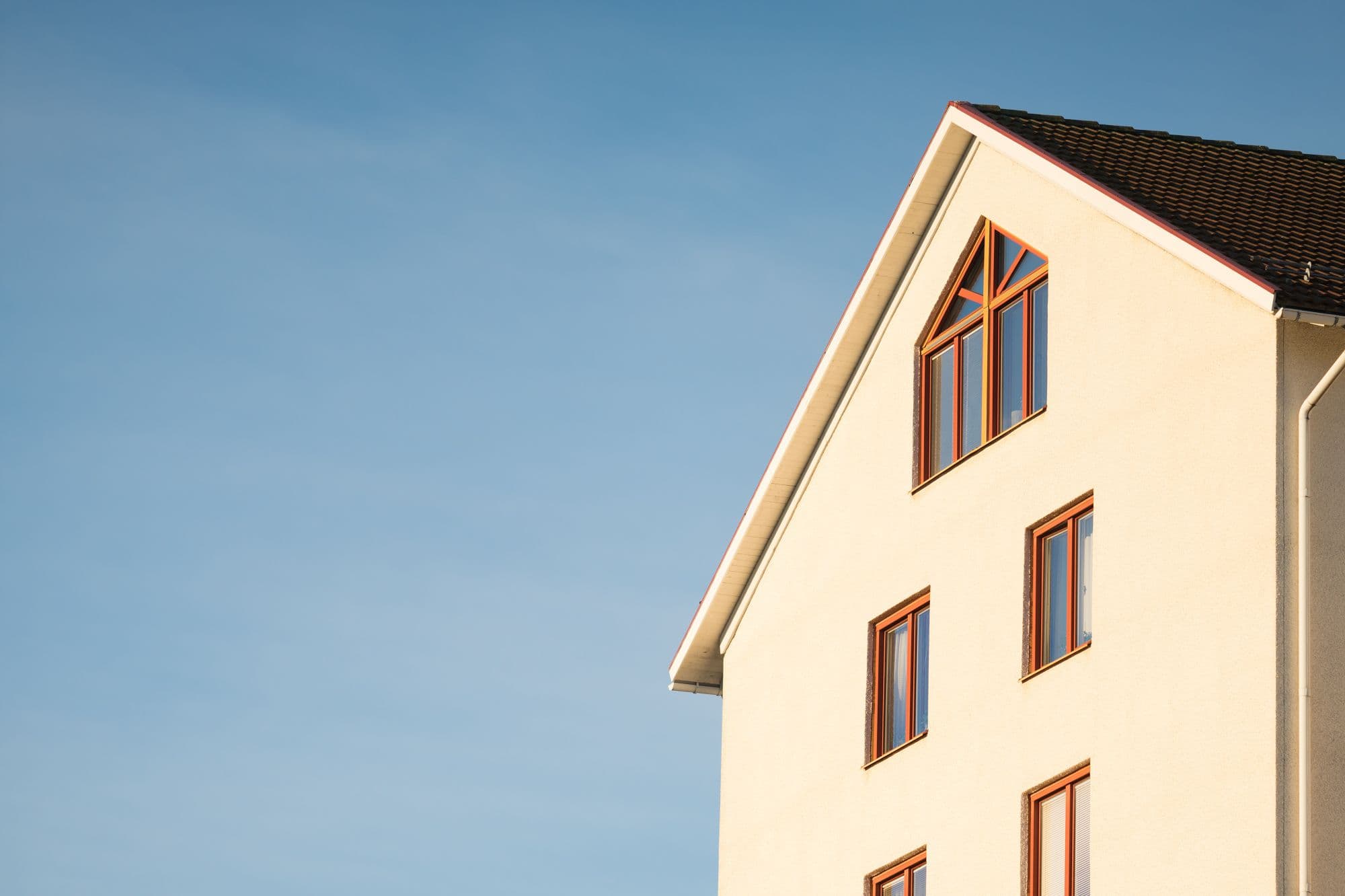 The gable end of a stucco home against a clear sky, with an upper-story window well above ladder height